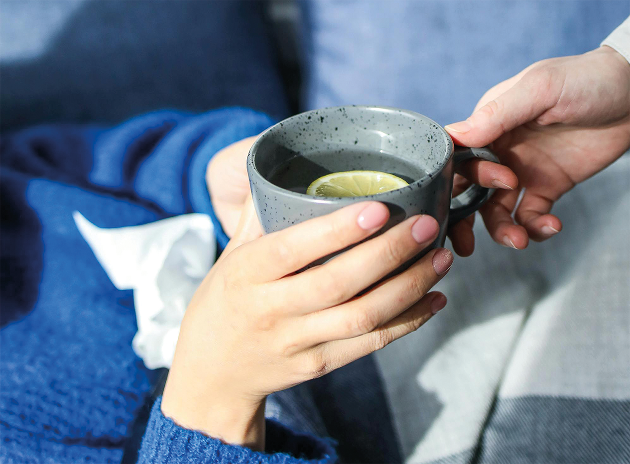 Eine Person übergibt einer anderen Person ein Heißgetränk mit Zitrone in einer Tasse