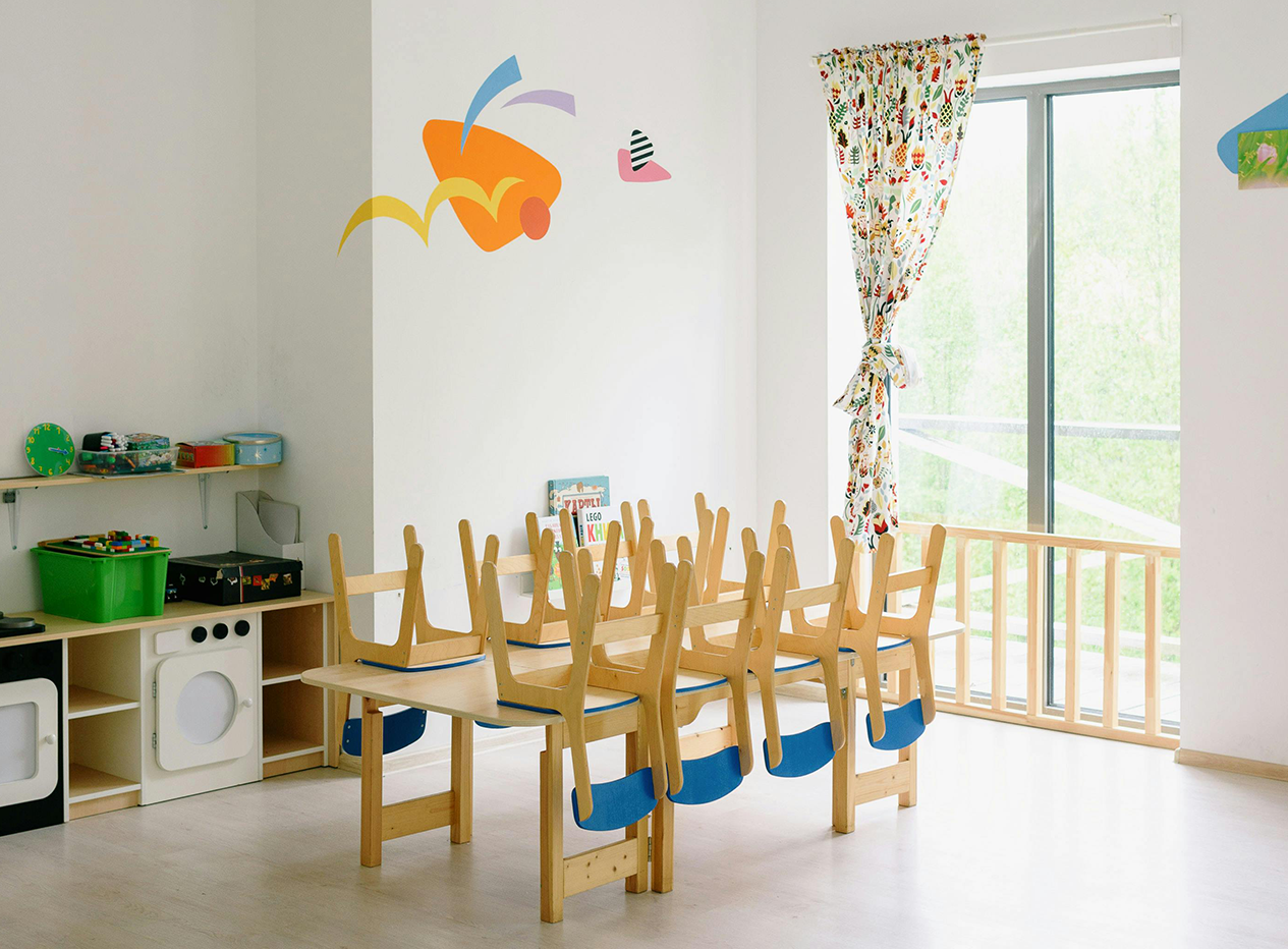 Ein Raum eines Kindergartens in dem ein Tisch mit hochgestellten Stühlen sowie Regale mit Spielsachen sind.