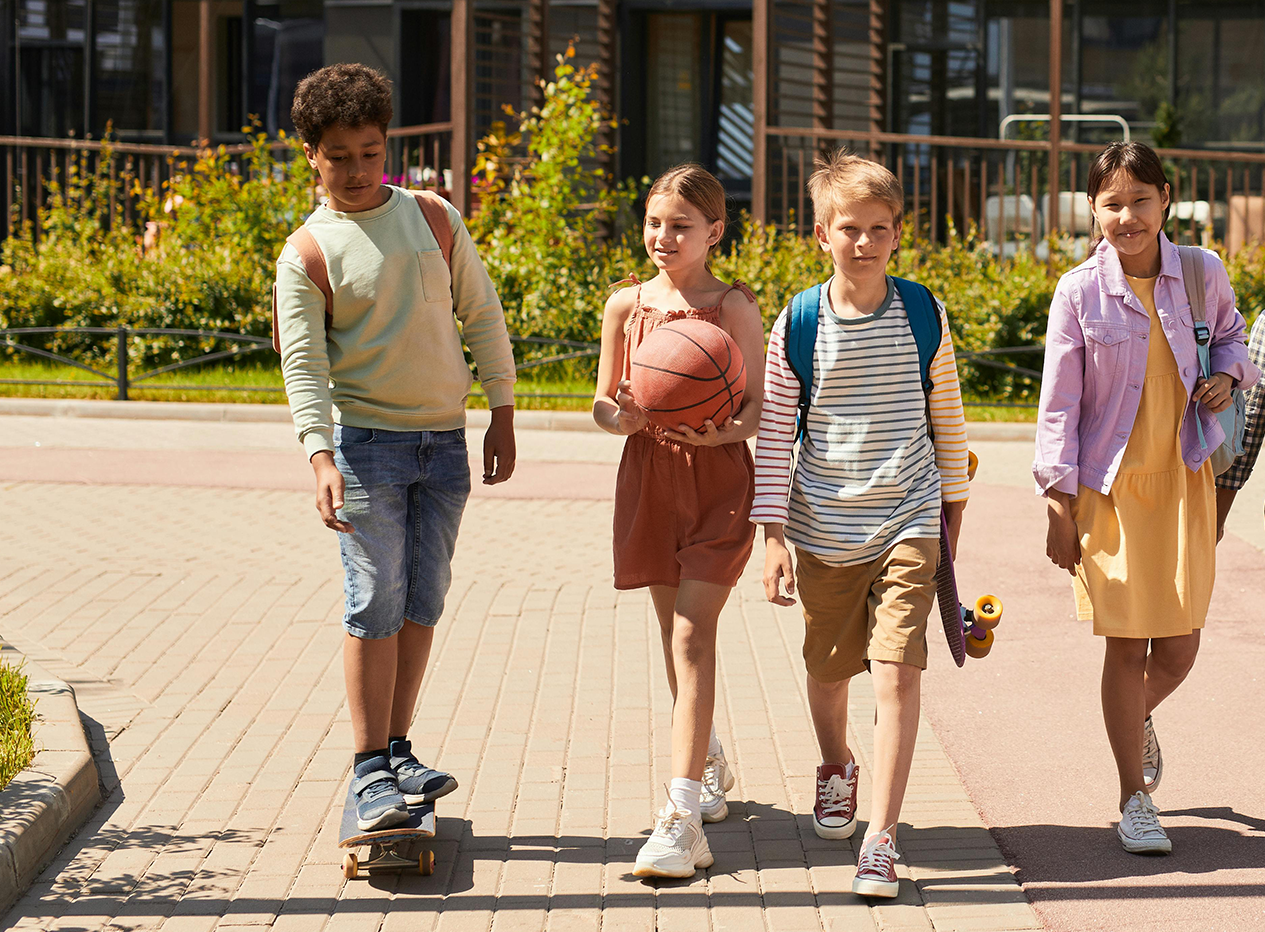 Vier Kinder gehen mit Basketball und Skateboard nebeneinander.